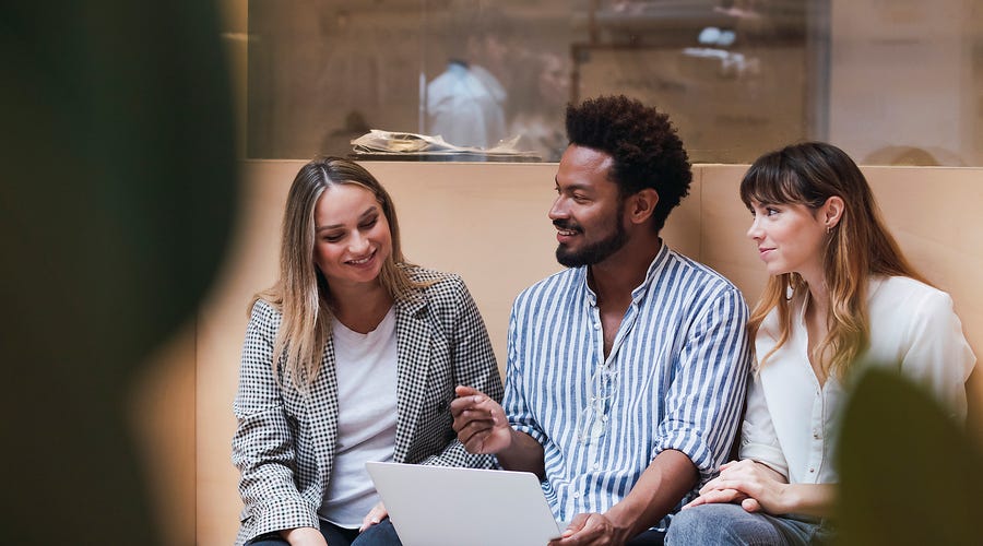 Um time de 3 pessoas, um rapaz e duas moças, que trabalham em uma empresa internacional, conversando em inglês.