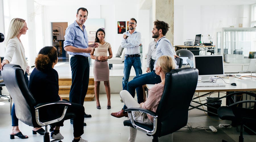 Equipe de pessoas vestindo trajes corporativos em uma reunião descontraída no escritório.