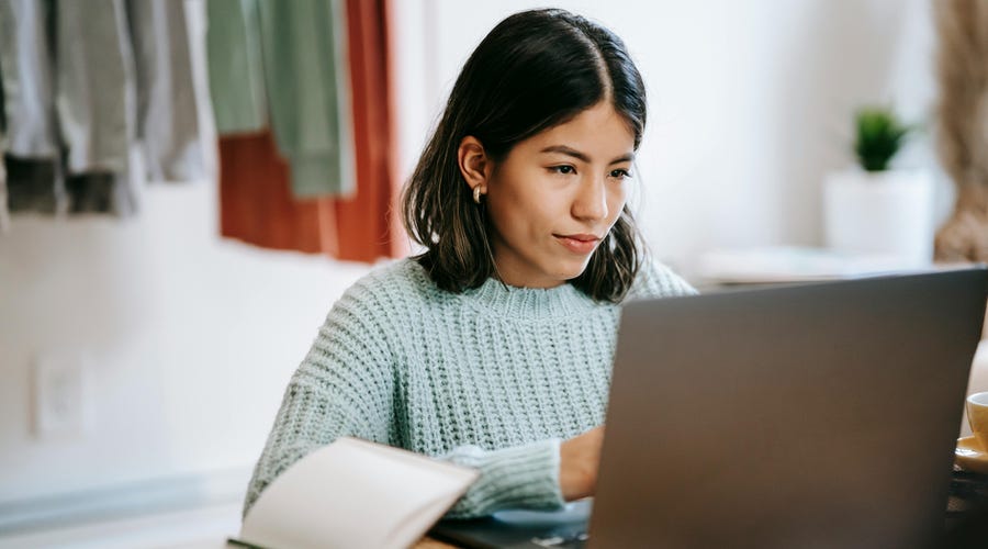 Mulher de cabelos escuros em frente a um laptop provando que a aula experimental é um ótimo teste de metodologia.