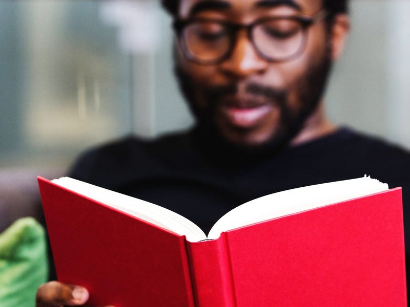 Homem negro de óculos lendo um livro de capa vermelha.