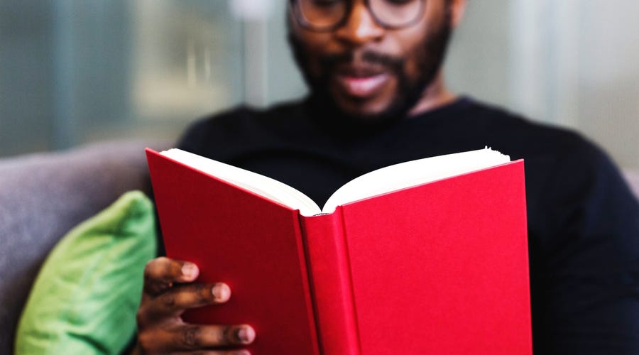 Homem negro de óculos lendo um livro de capa vermelha.
