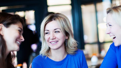 Três mulheres sorrindo enquanto conversam em uma mesa de restaurante.