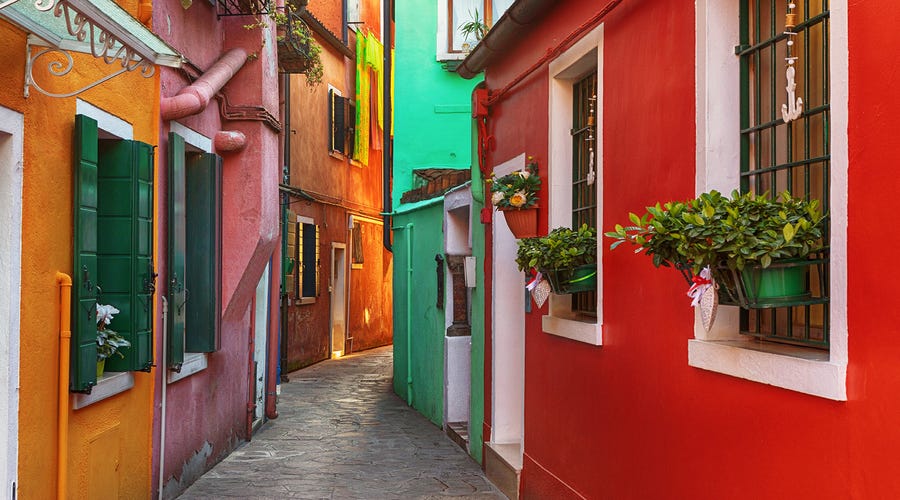 Rua estreita com casas coloridas e floreiras, comum em países que falam espanhol. 