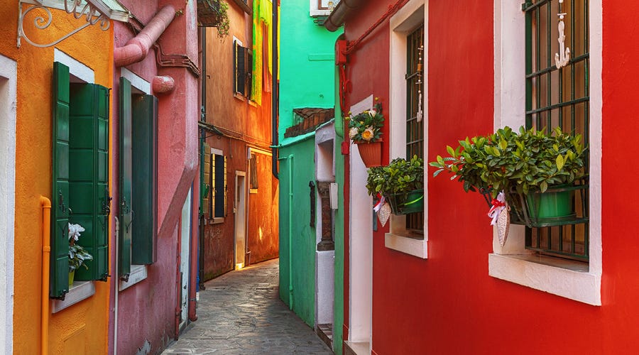Rua estreita com casas coloridas e floreiras, comum em países que falam espanhol. 