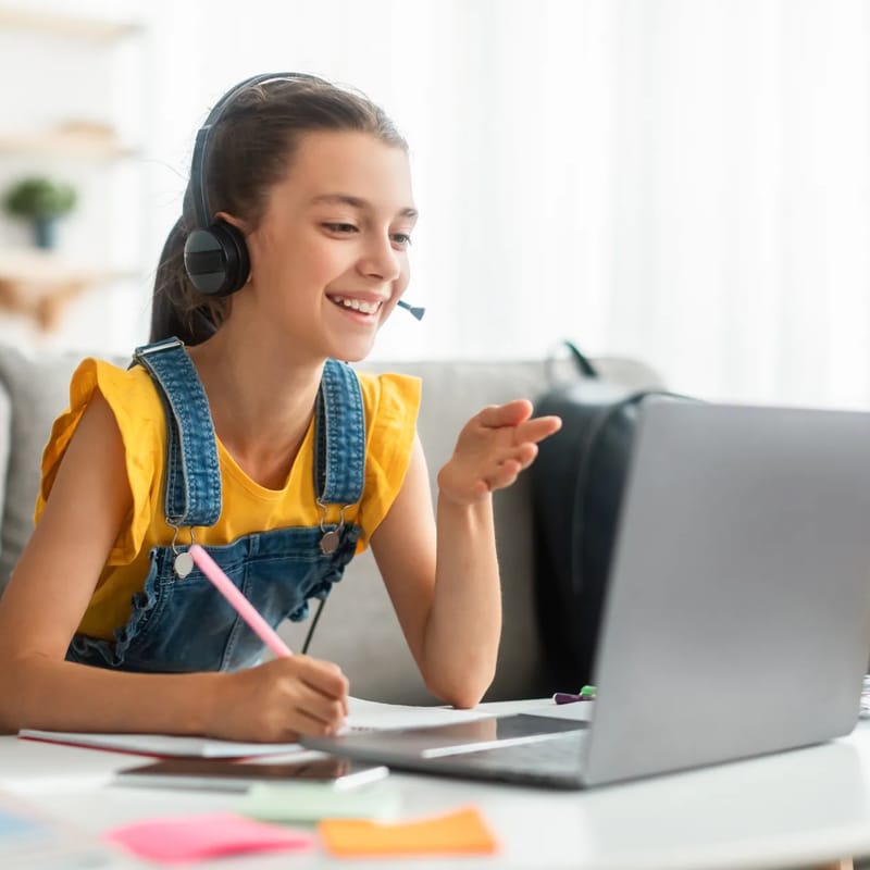 Menina sentada com laptop aprendendo espanhol online para crianças.