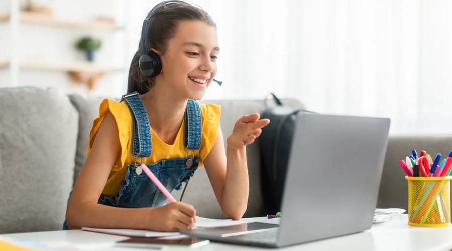 Menina sentada com laptop aprendendo espanhol online para crianças.