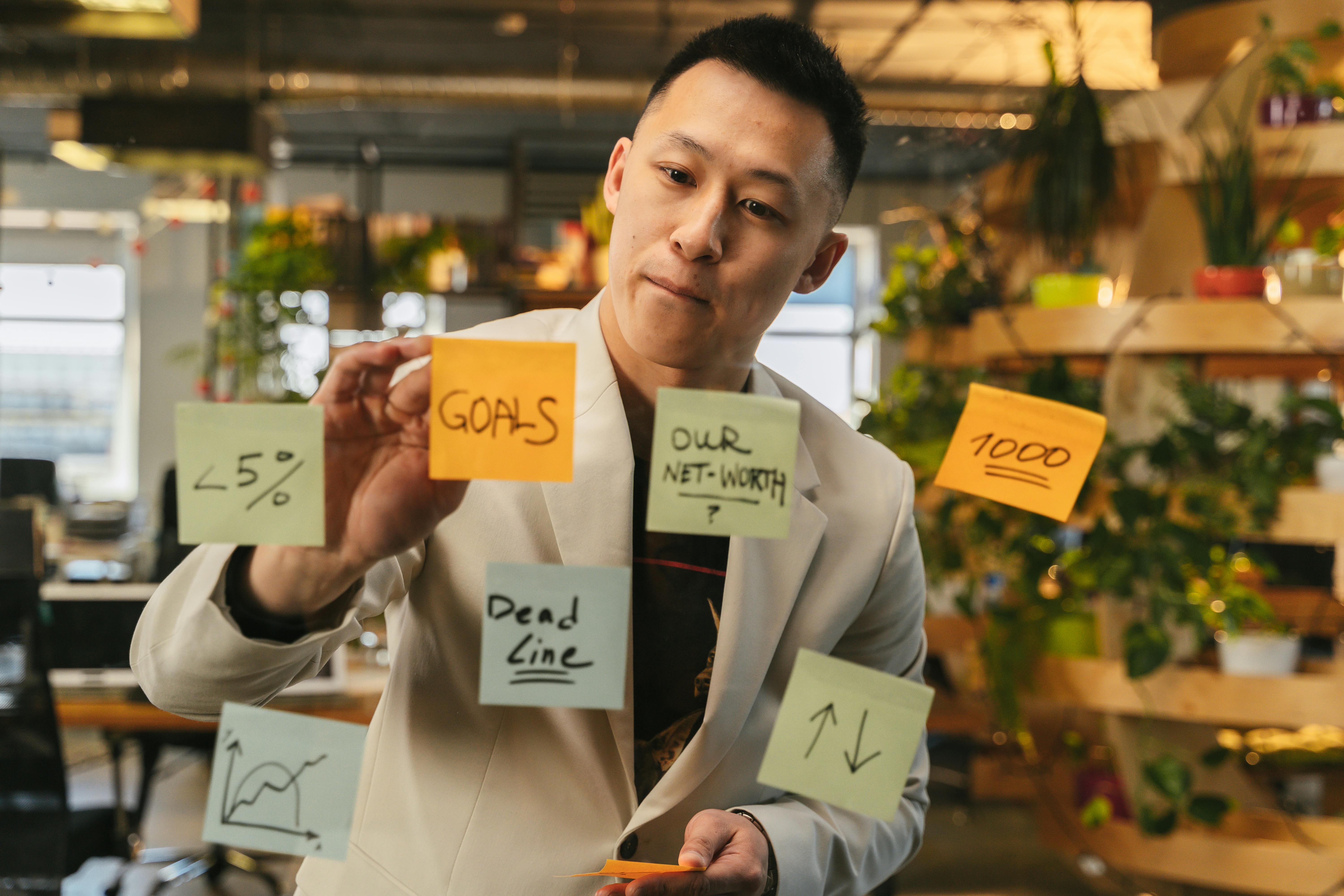 Homem organizando suas demandas em post-its sobre uma parede de vidro para visualizar melhor sua gestão de tempo.