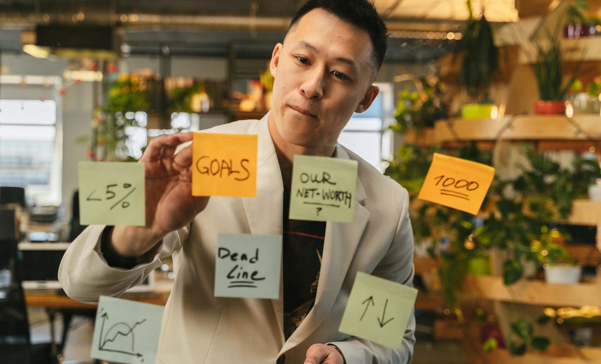 Homem organizando suas demandas em post-its sobre uma parede de vidro para visualizar melhor sua gestão de tempo.