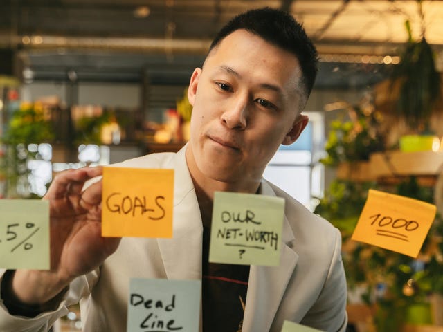 Homem organizando suas demandas em post-its sobre uma parede de vidro para visualizar melhor sua gestão de tempo.