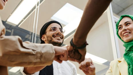 Colaboradores em roda unindo as mãos no centro enquanto comemoram a conscientização cultural na empresa.