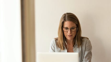 Mulher de fones usando um laptop sentada em uma mesa.
