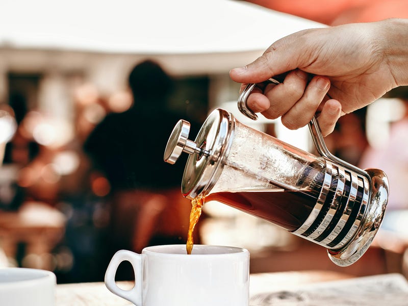 Garçom servindo café em uma xícara diretamente de uma prensa francesa para um cliente que aprendeu como pedir um café em francês.