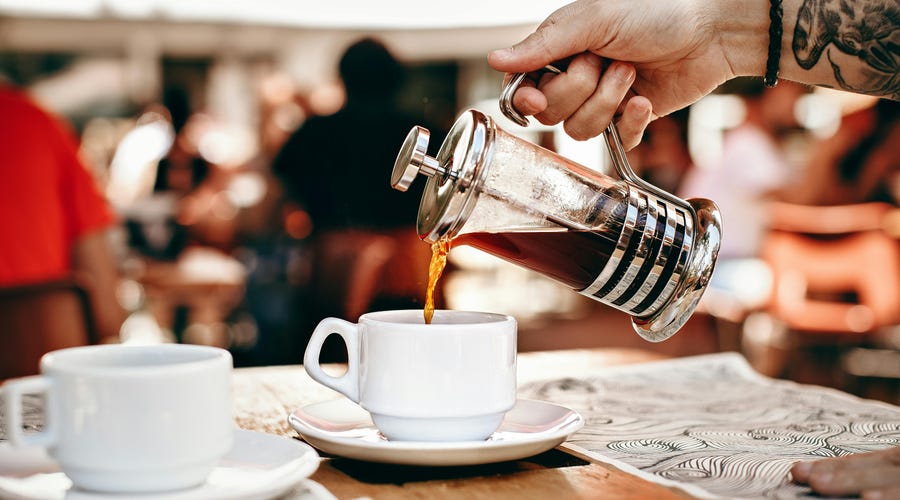 Garçom servindo café em uma xícara diretamente de uma prensa francesa para um cliente que aprendeu como pedir um café em francês.