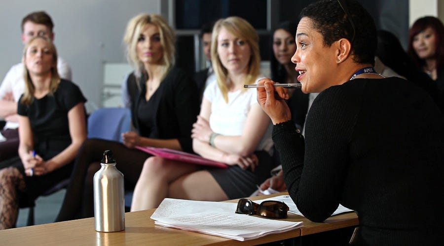 Mulher realizando uma apresentação enquanto uma plateia de mulheres assistem.