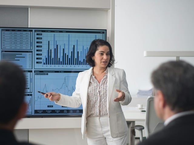 Mulher que fez o curso de liderança do Berlitz realizando uma apresentação em slides com gráficos para diversas pessoas.