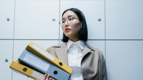 Mulher asiática em pé vestida com roupas formais segurando pastas coloridas com documentos sobre cultura da responsabilização.