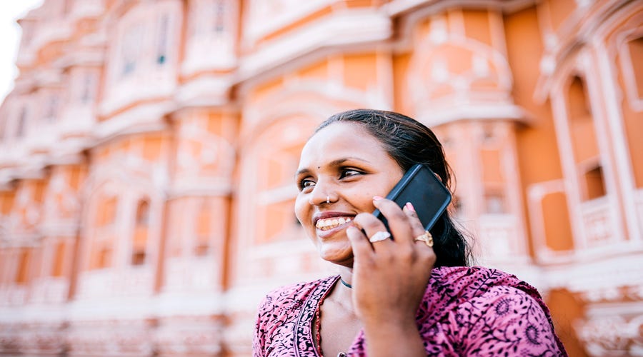 Mulher indiana falando ao telefone enquanto utiliza o que aprendeu na aula de "olá" em várias línguas.