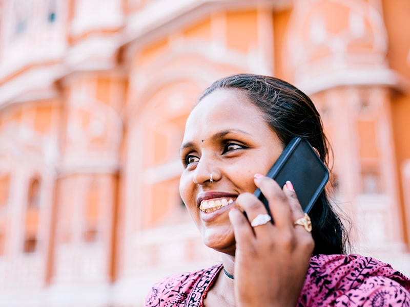 Mulher indiana falando ao telefone enquanto utiliza o que aprendeu na aula de "olá" em várias línguas.