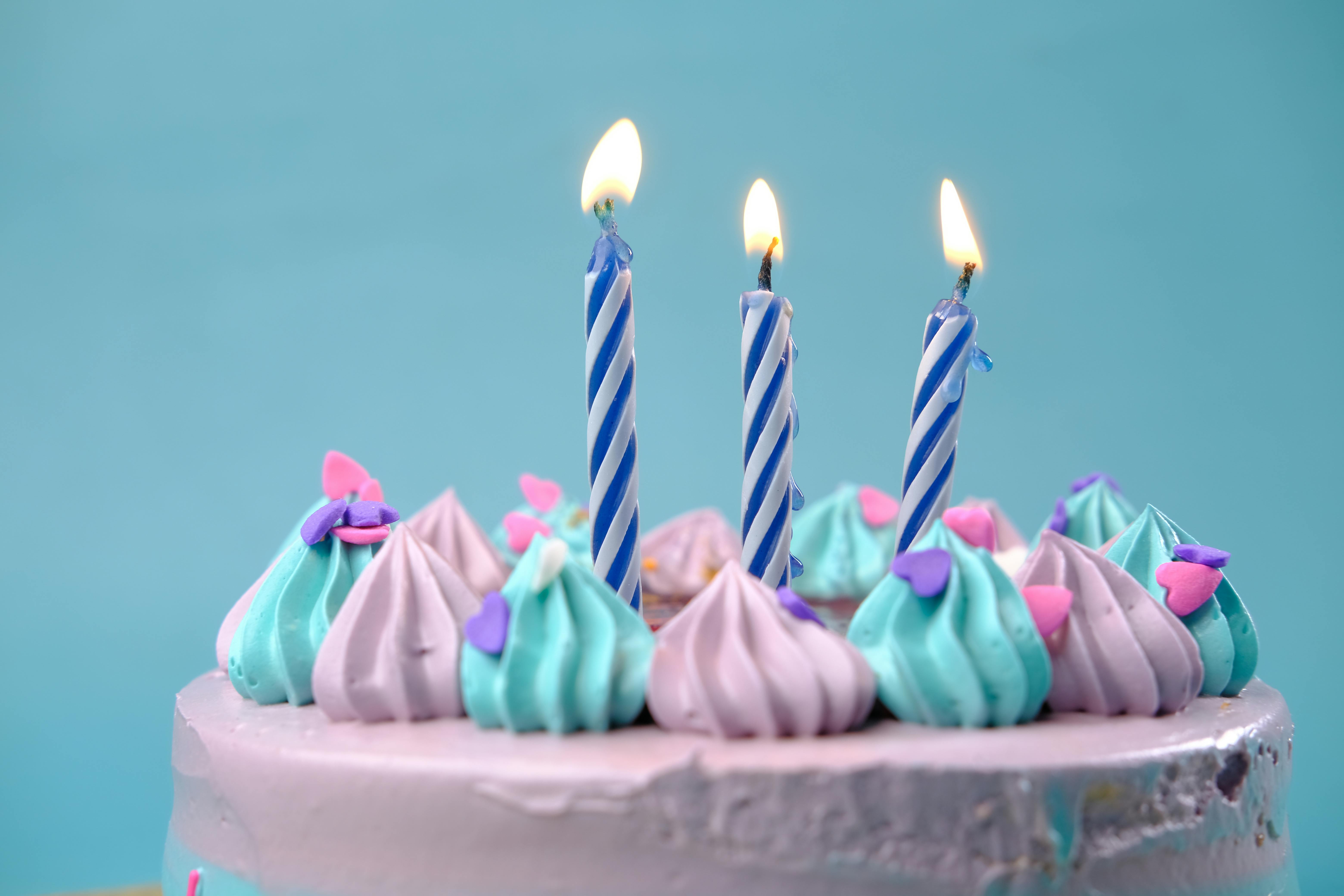 Bolo de feliz aniversário em italiano com velas acesas e confeitos.