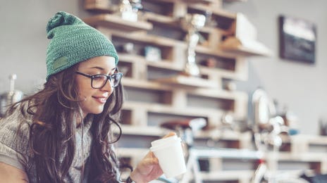 Mulher usando uma touca verde tomando café mexendo em um laptop.