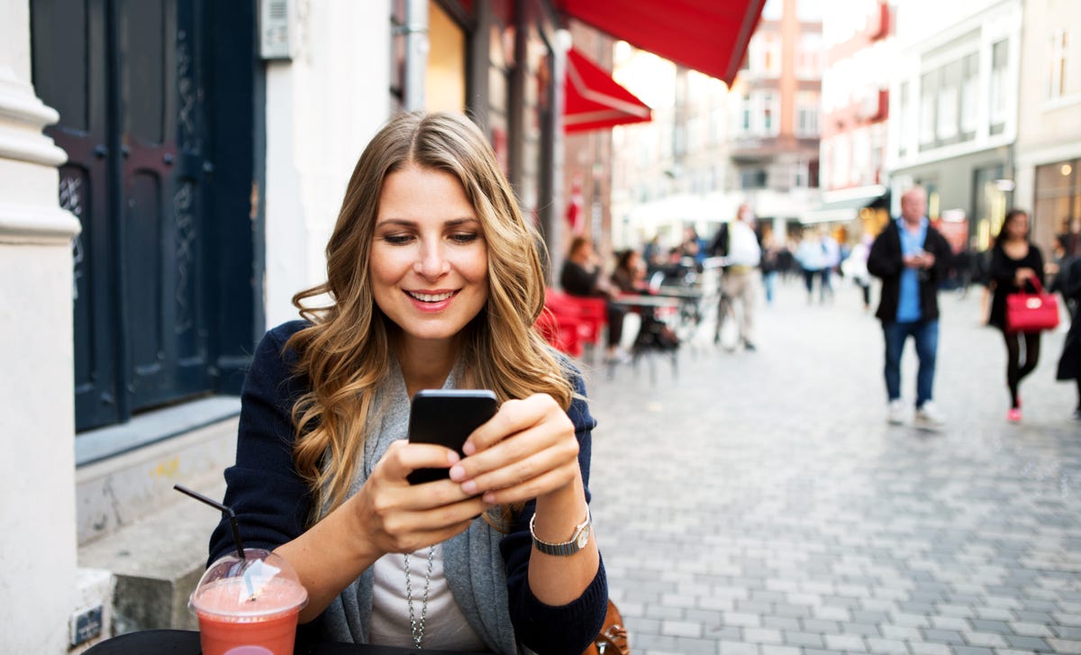 Mulher mexendo no celular sentada em uma mesa enquanto toma milkshake.