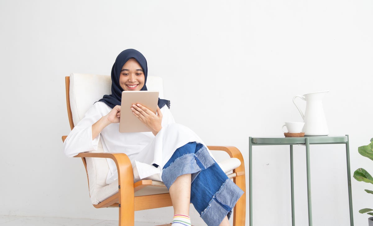 Woman in a scarf holding a tablet and contacting Berlitz while smiling