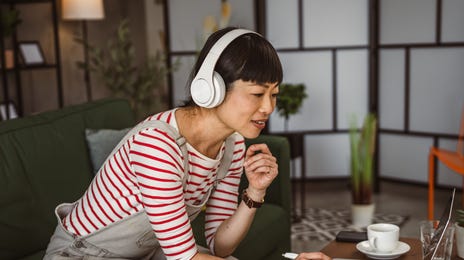 Woman in headphones sitting on her couch and talking to her instructor during an online group language lesson with Berlitz Saudi Arabia