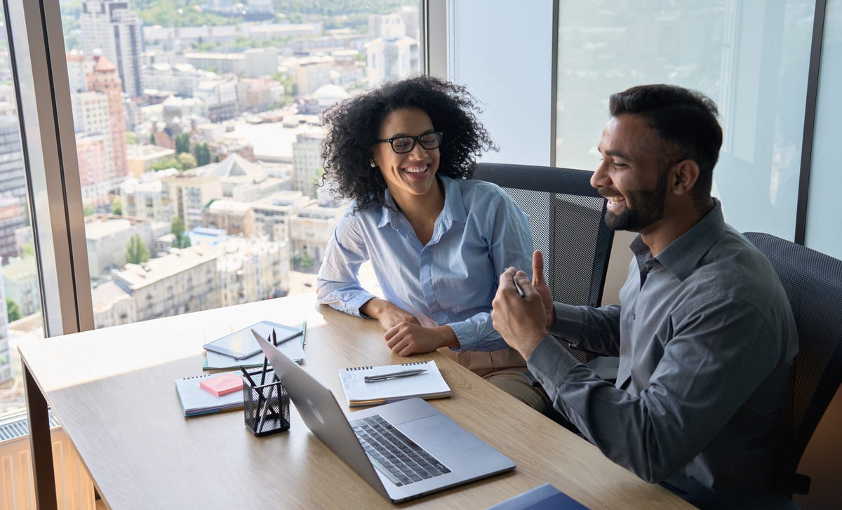 Two students sitting at a table in front of a laptop and chatting happily after their Spanish speaking course