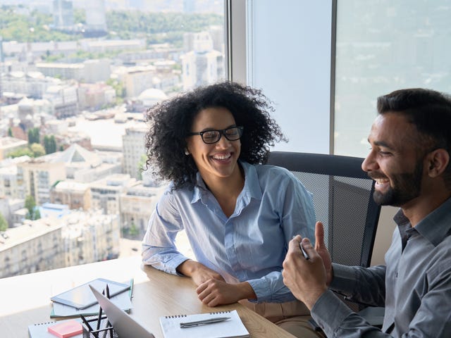 Two students sitting at a table in front of a laptop and chatting happily after their Spanish speaking course