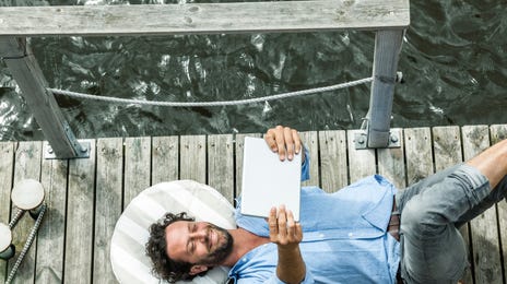 Man on a beach holding his tablet and learning a language with Berlitz Flex