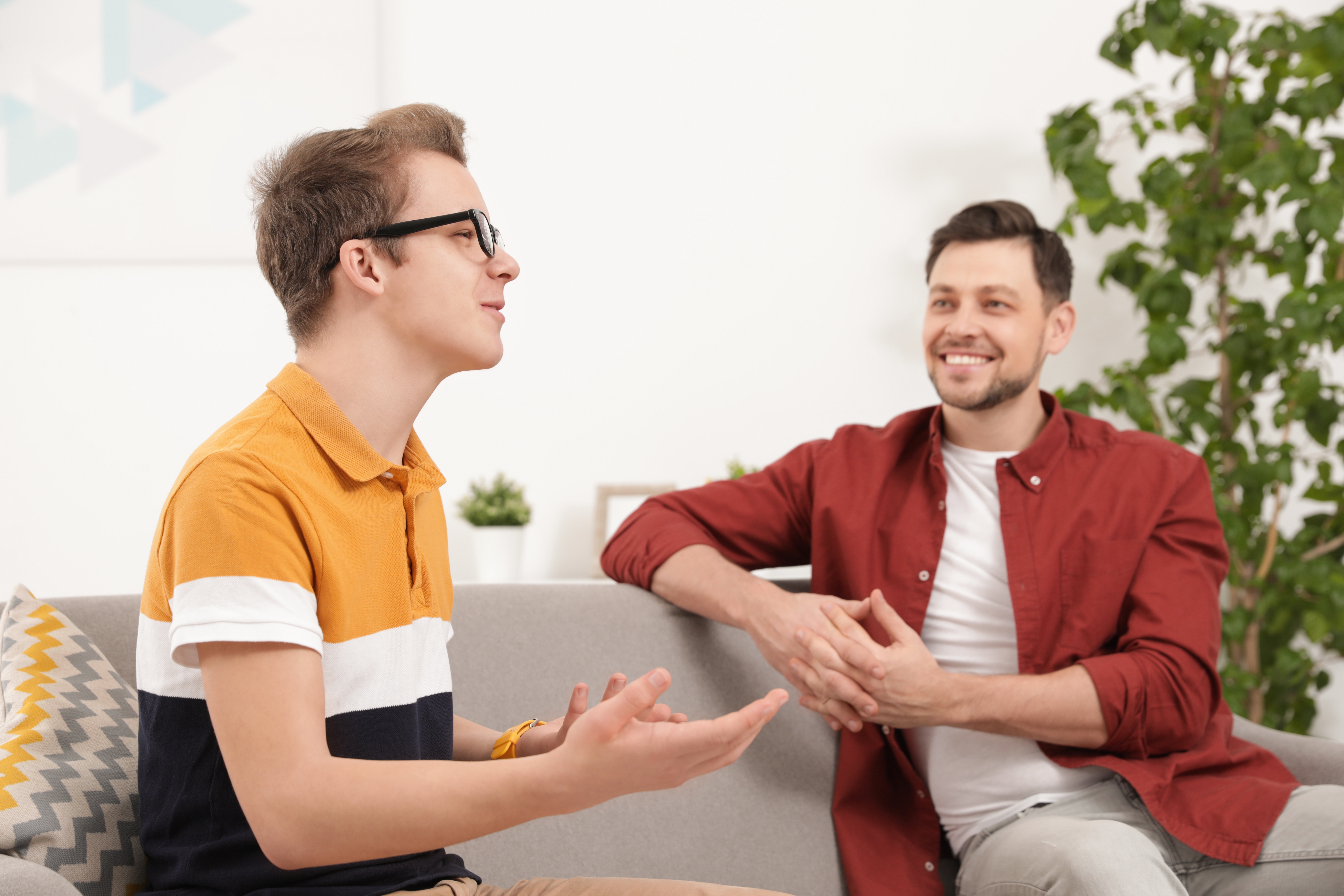 Teenager sitting on a couch and talking to his instructor in a foreign language during their private lesson for young learners