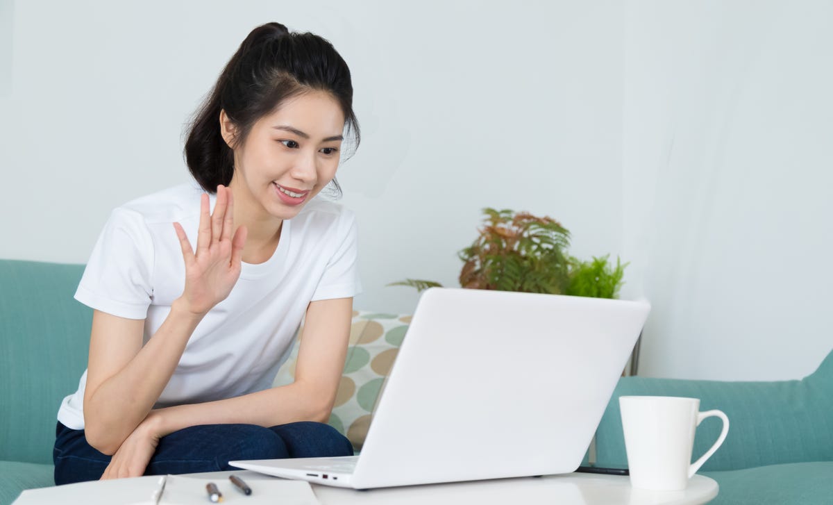 Woman attending her Portuguese speaking course from her laptop and waving at her instructor