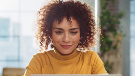 Woman in a yellow shirt checking out online language classes for adults with Berlitz on her laptop