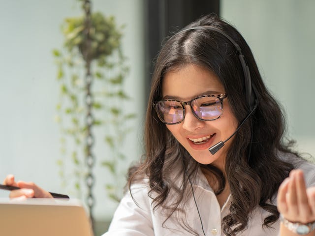 Woman in headphones looking at her laptop screen and talking to her instructor during one of her private language courses online