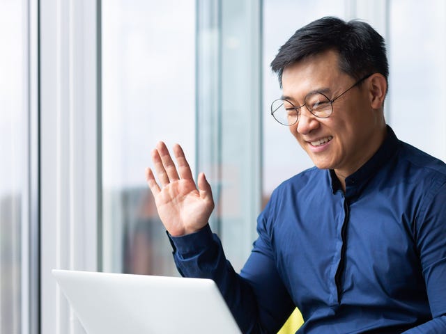 Man in glasses holding his laptop and waving at his instructor at the beginning of his online private language lessons with Berlitz Saudi Arabia