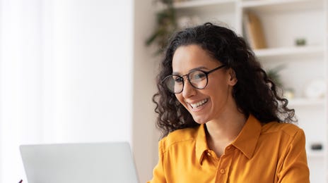 Woman in a yellow shirt smiling in front of her laptop and e-learning languages online with Berlitz