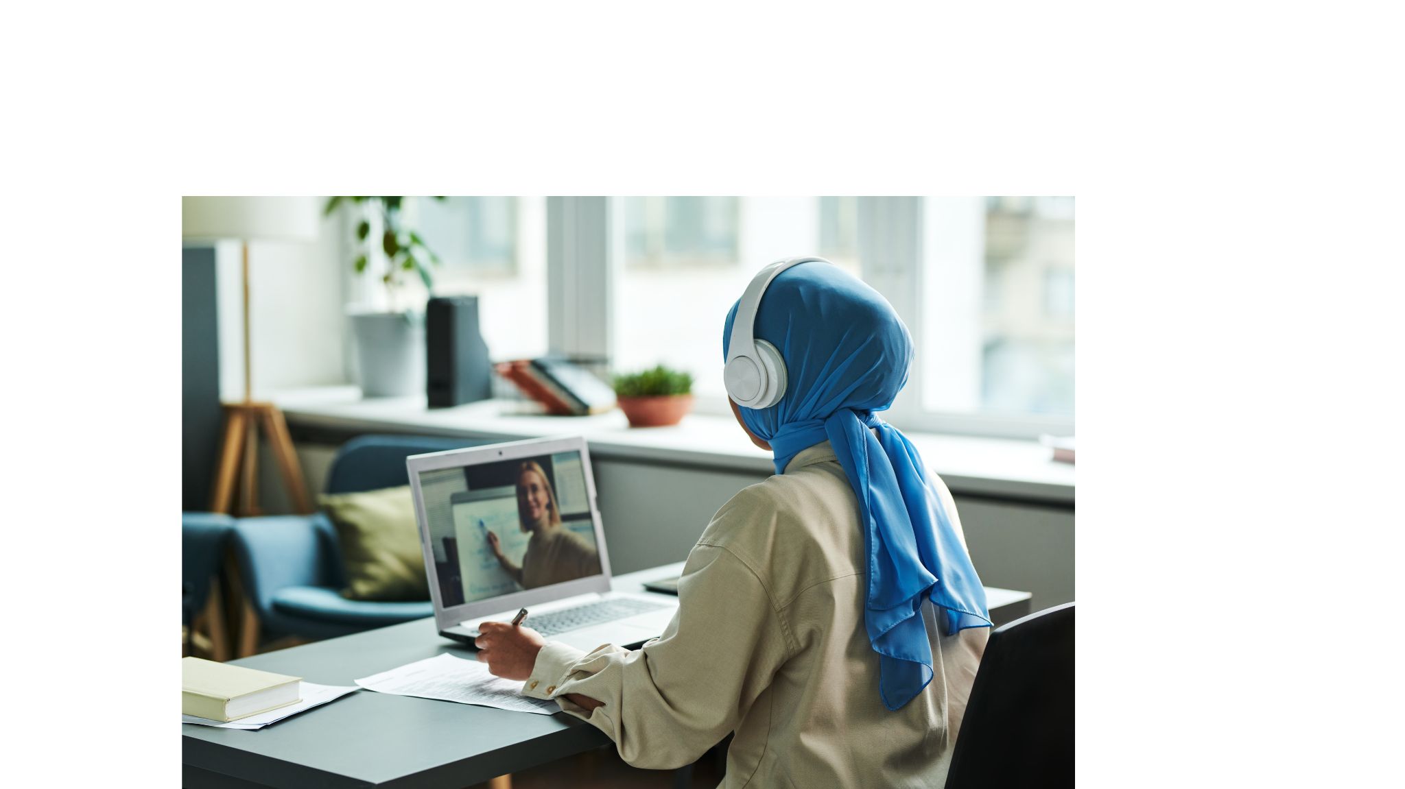 Woman sitting at a desk talking to her instructor during an online private language class on her laptop