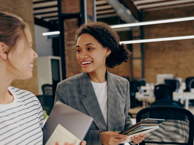 Coworkers in an office holding documents and talking happily after their Total Immersion language program