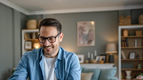 Man sitting at a table in his living room and attending private language courses online from his laptop