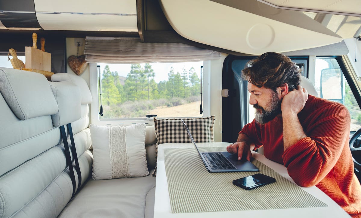 Man in a van sitting at a table and reading Saudi Arabia's Imprint on his laptop