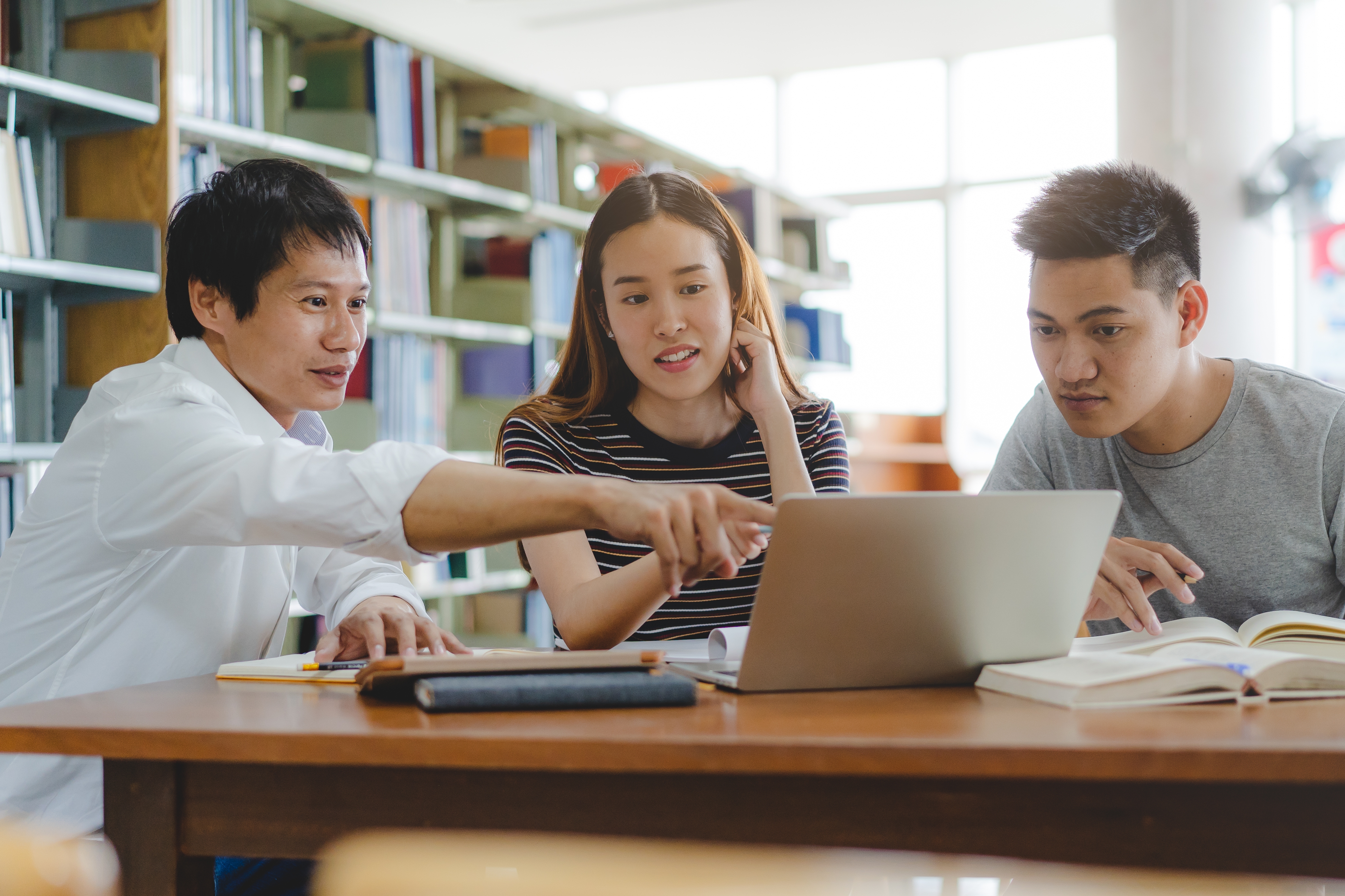 Teenagers sitting in a library and looking at a laptop screen together after one of their French courses for teens with Berlitz Saudi Arabia