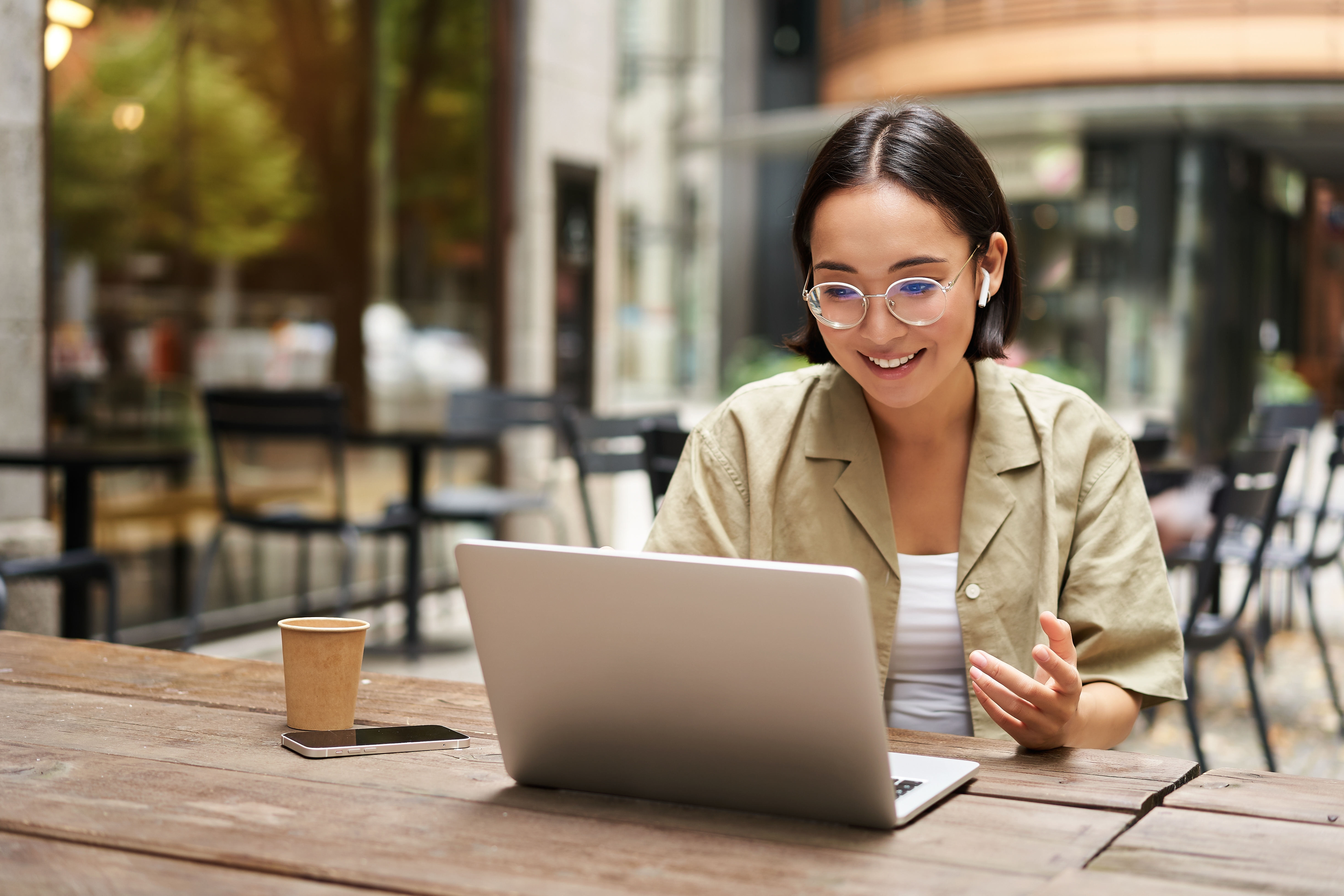Woman sitting outside on a bench with her coffee and laptop and learning a new language with Berlitz Flex