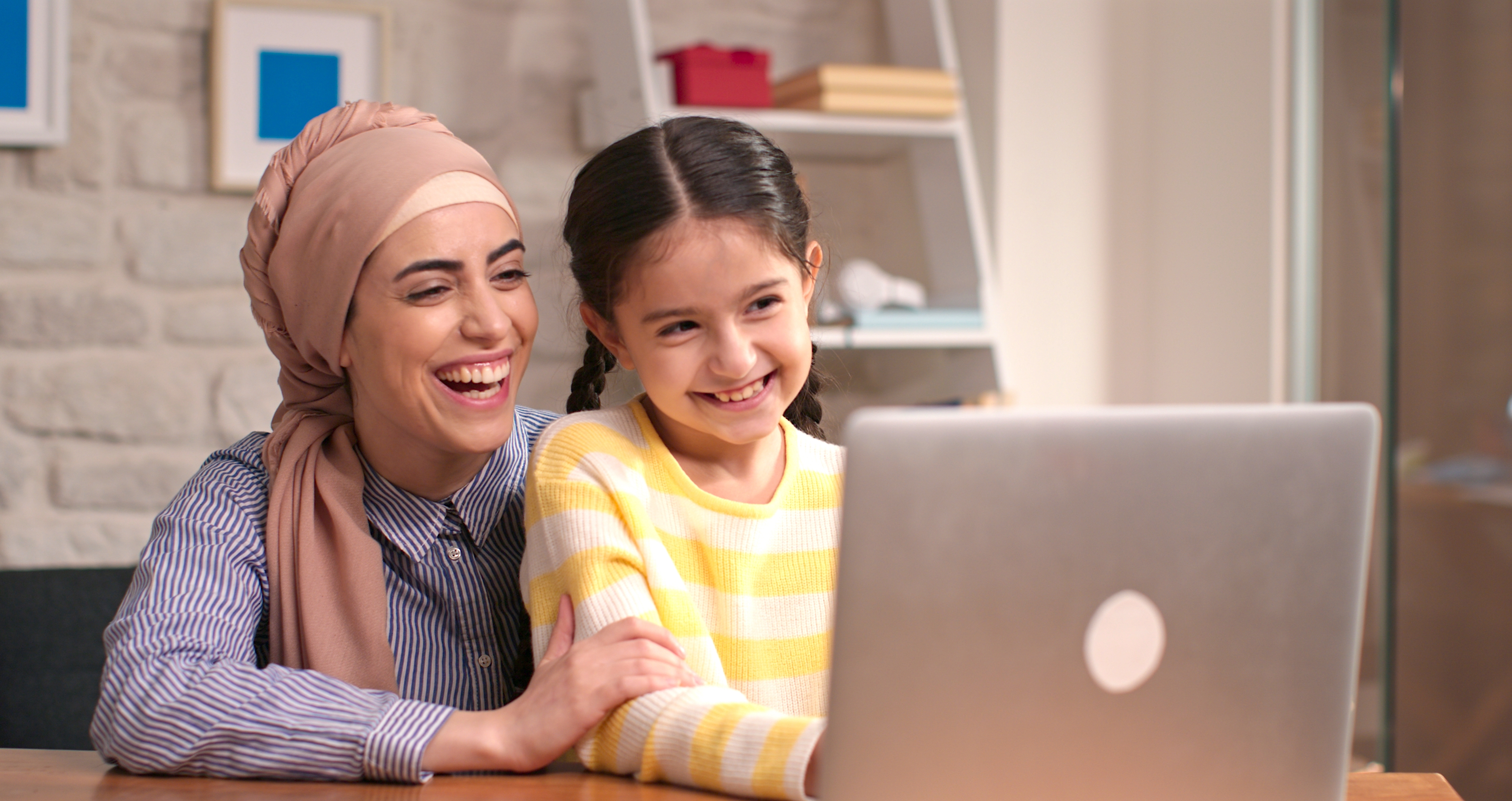 Little girl and her instructor looking at the laptop screen and smiling while practicing the language during an English course for young learners
