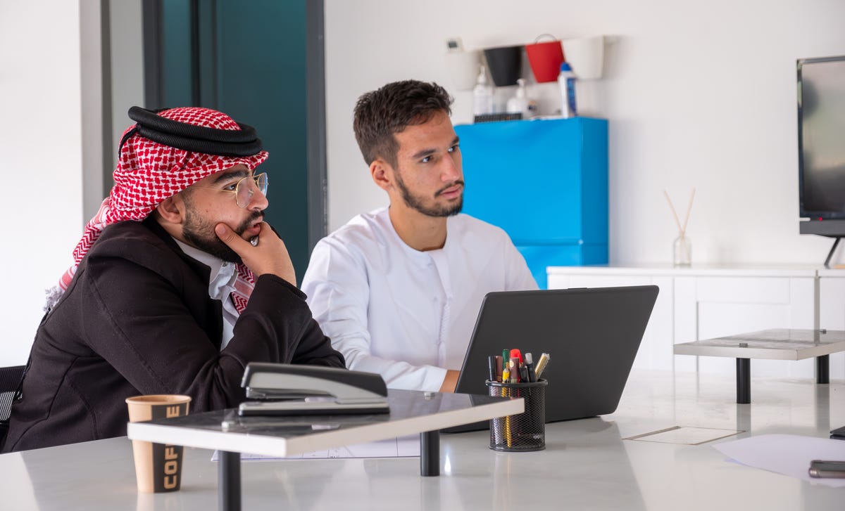 Two men sitting in front of a laptop and learning about why it is beneficial to learn a language with Berlitz