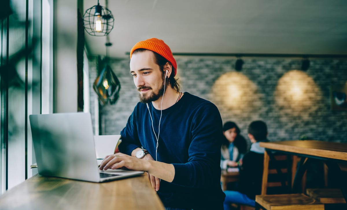 Man in a hat sitting in a coffee shop and completing the Berlitz placement test on his laptop to find out his language level