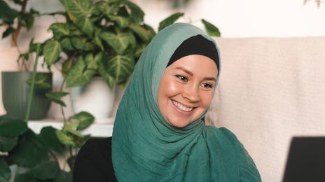 Woman in a scarf smiling at her laptop screen during her online language lesson with Berlitz Saudi Arabia