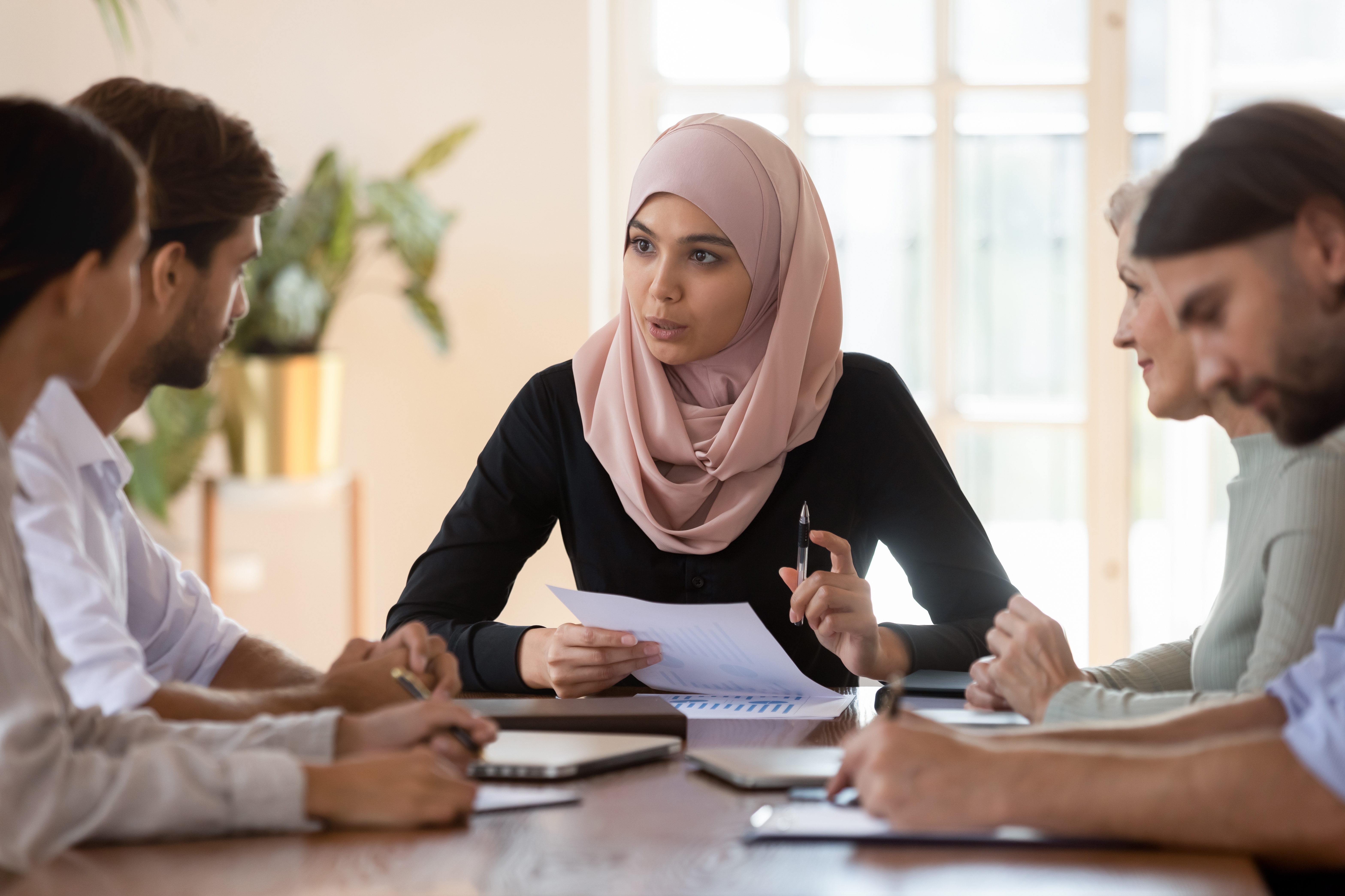 Woman in scarf holding a piece of paper and a pen and talking to her classmates during a group language lesson with Berlitz Saudi Arabia
