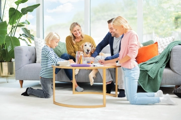 Family and dog sitting around table on carpet in living area.