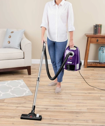 Person carrying Zing Bagged Canister Vacuum around room.