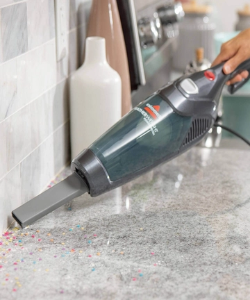 Using Featherweight Stick Vac has hand vac with crevice tool vacuuming couch cushions 